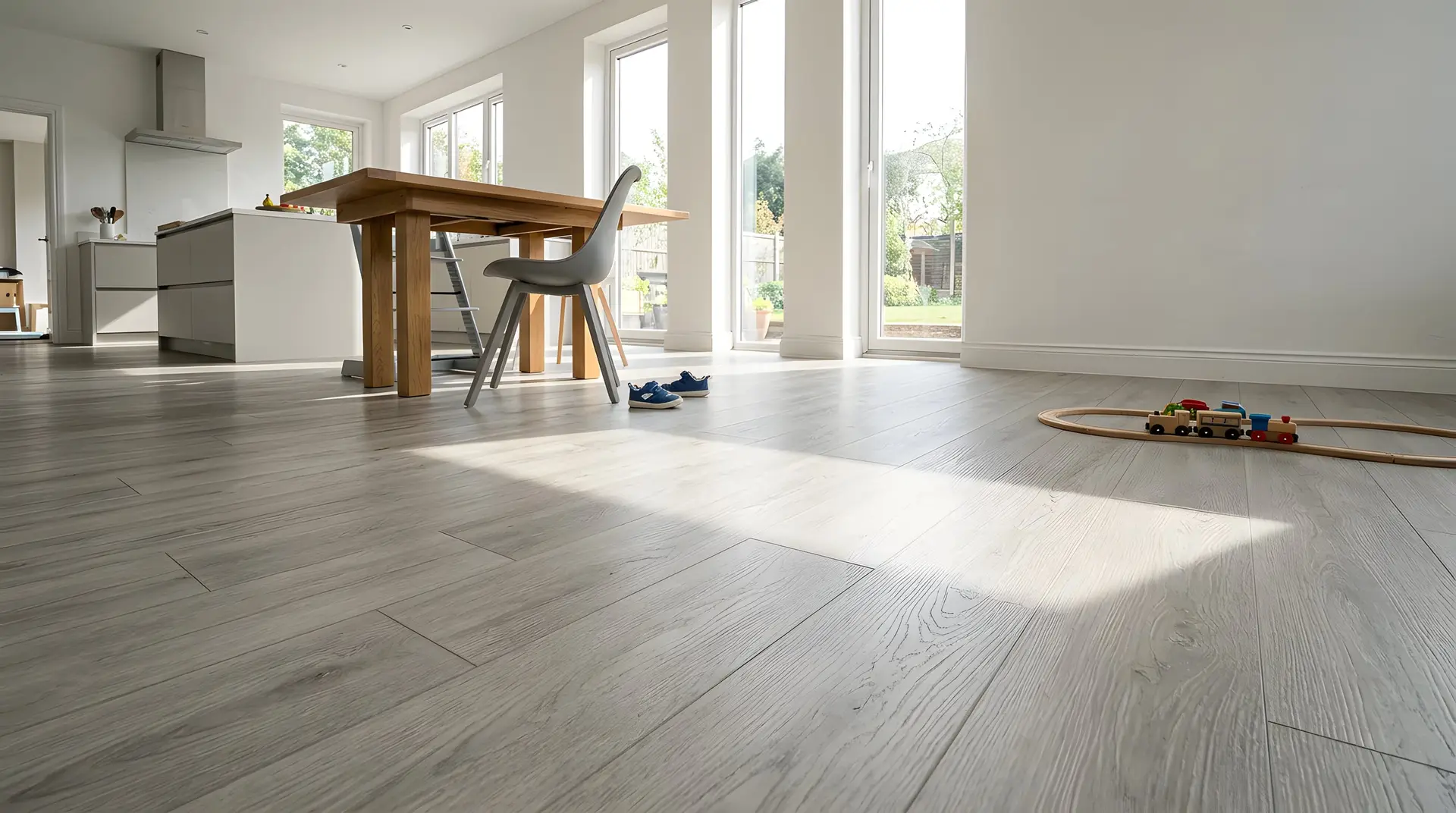 Grey laminate flooring through a bright open kitchen and dining room, a toy train on the floor