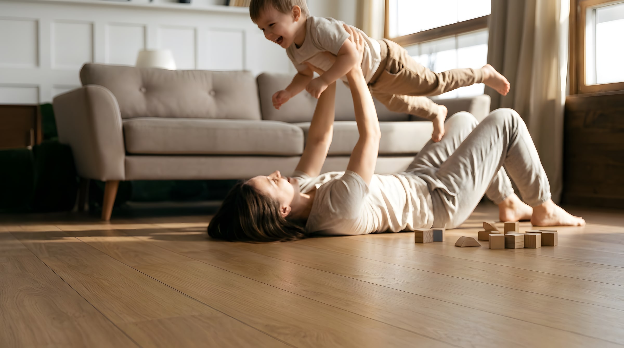 A parent lying on a warm oak floor lifting a laughing child airplane-style